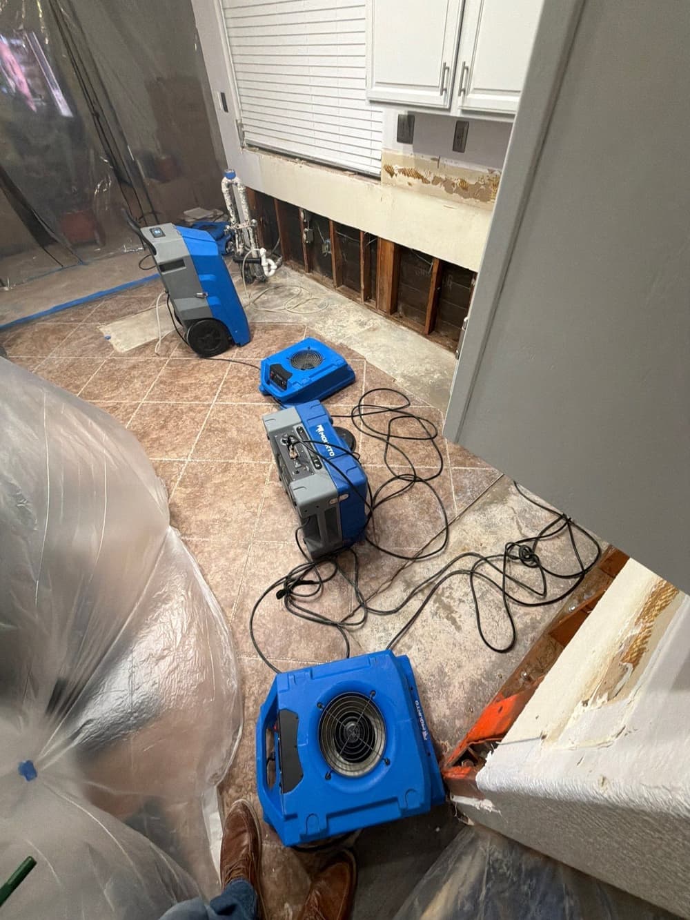 Air movers and a dehumidifier running against a flood-cut kitchen wall on a Resolve Residential Restoration job