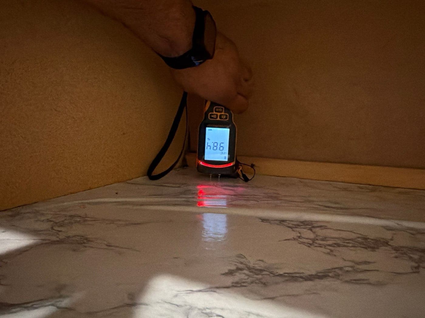 A Resolve Residential Restoration technician holding a pin-type moisture meter against a kitchen cabinet base during drying checks