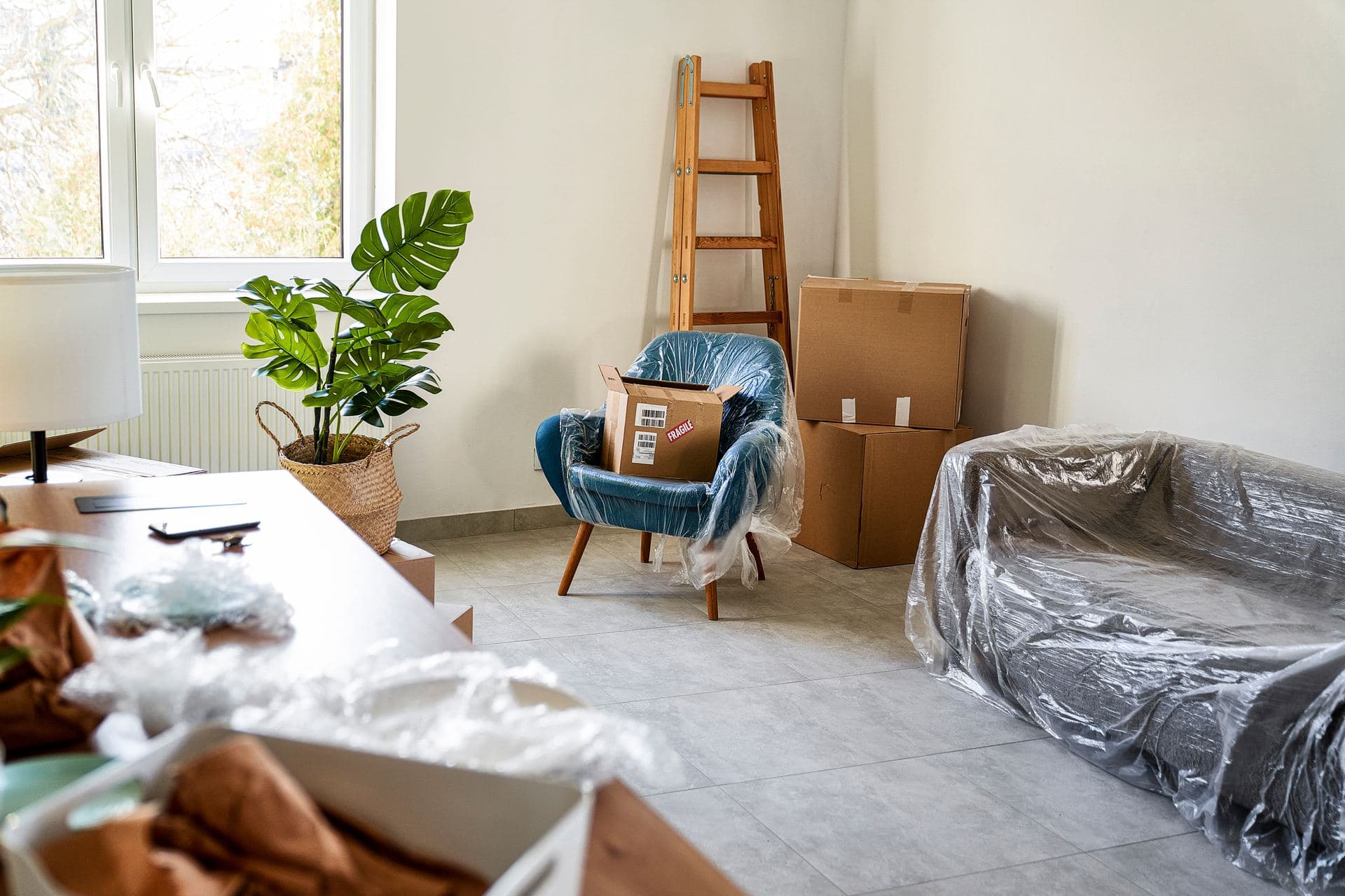 A living room mid pack-out with furniture covered in plastic and labeled boxes stacked