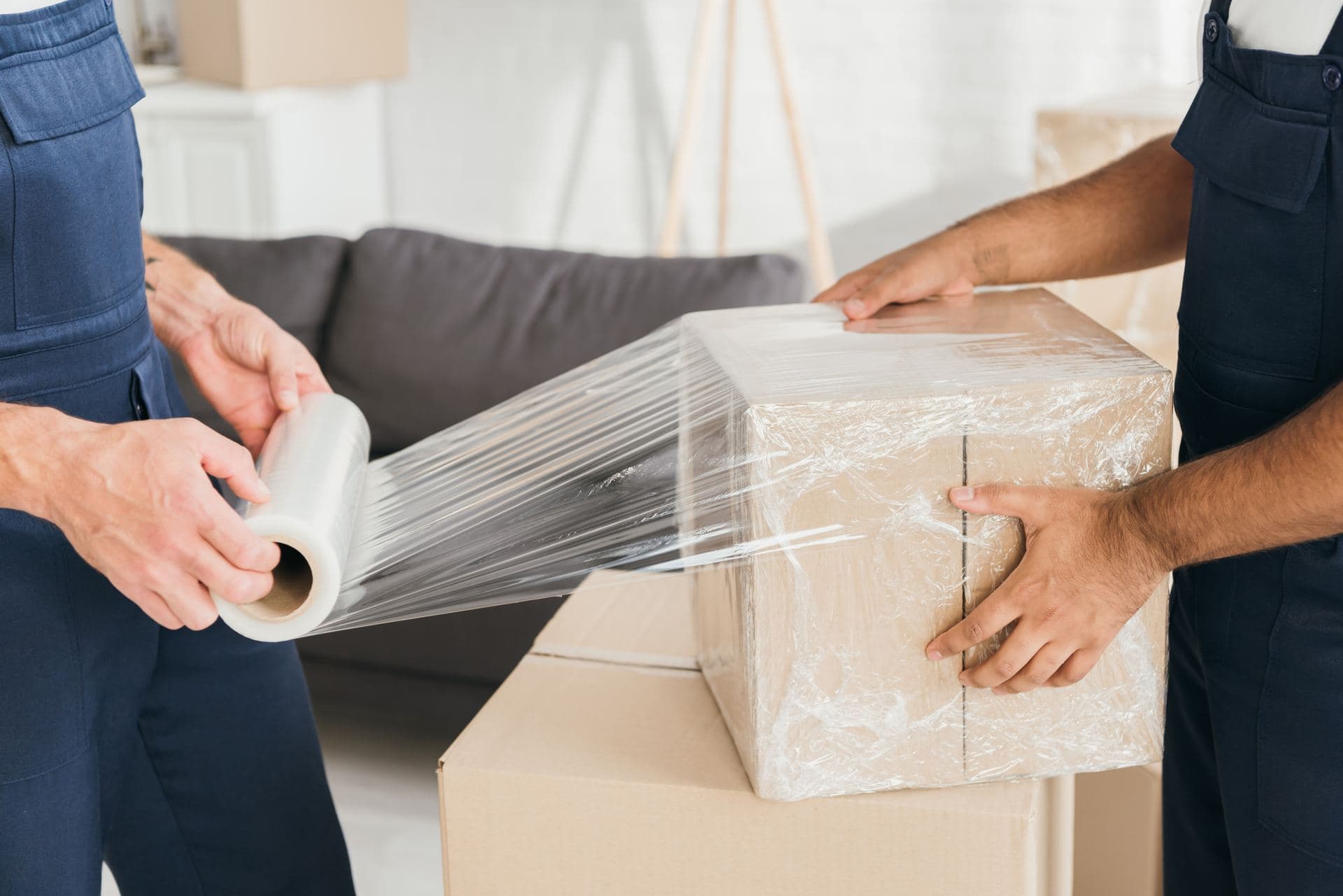 Movers wrapping a packed box in protective stretch film
