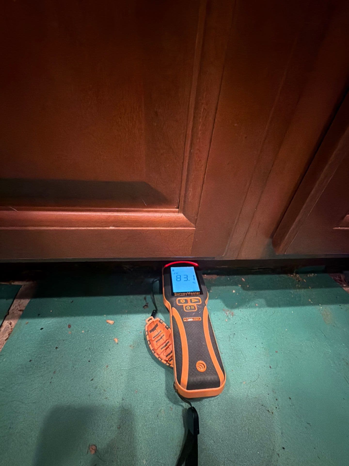 Protimeter moisture meter verifying a drying target at a cabinet base on a Resolve Residential Restoration job