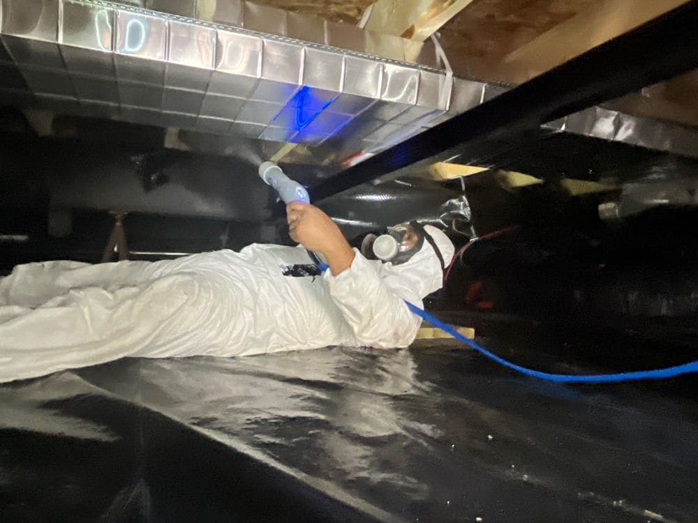 A Resolve Residential Restoration technician in full protective gear disinfecting a crawlspace after a sewage loss